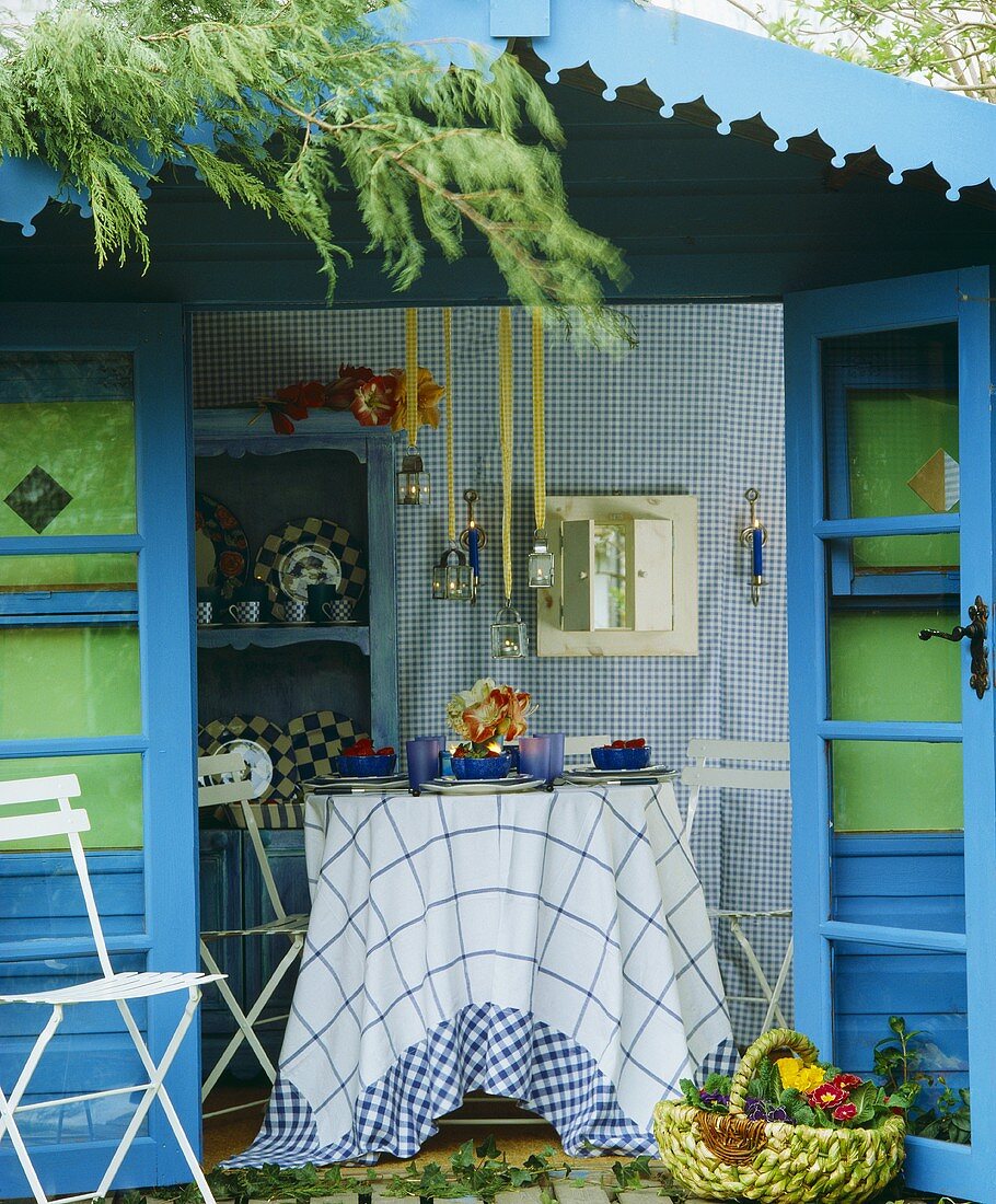 Blau gestrichenes Gartenhaus mit offenen Türen und und Blick auf gedeckten Tisch