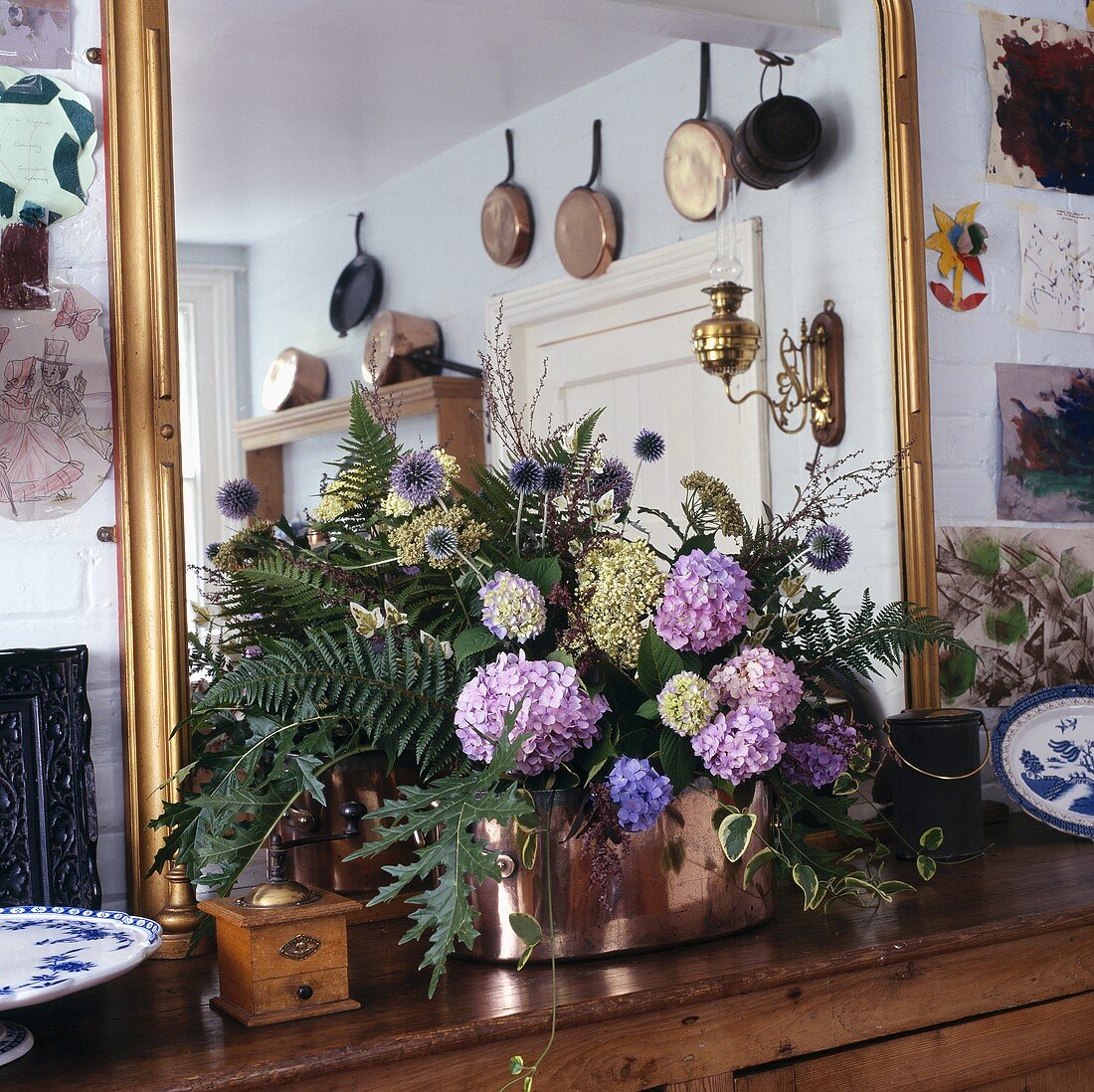 Lila Hortensien und Blätter in Kupferkrug vor großem vergoldetem Spiegel