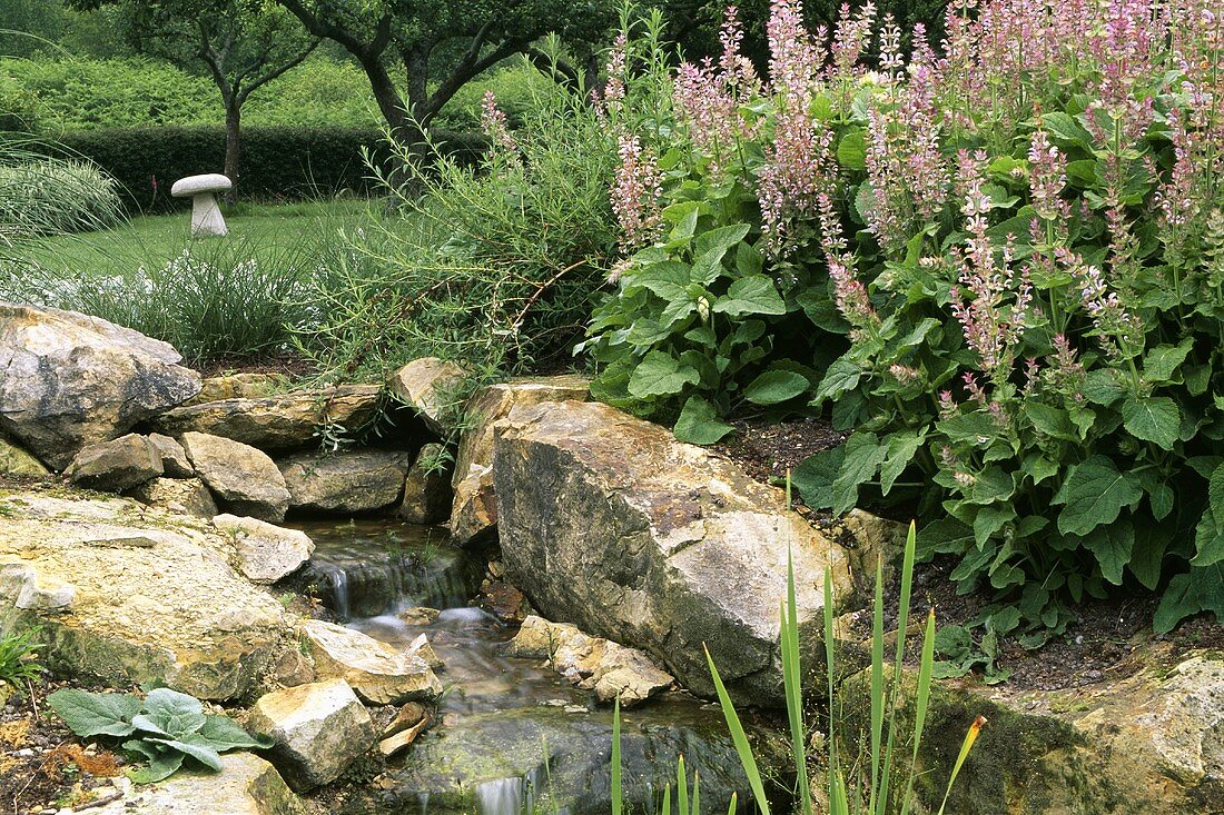 Kleiner Wasserfall mit Felsblöcken im blühenden Garten