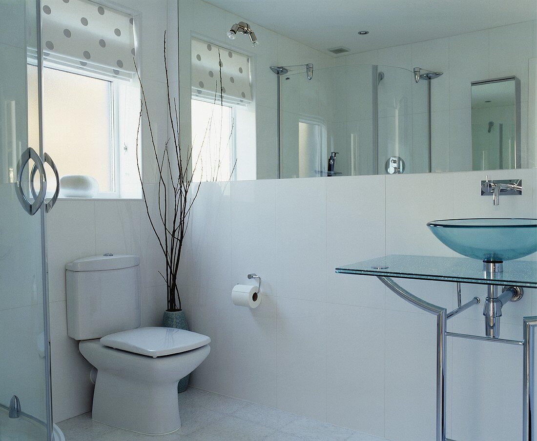 Modernes Badezimmer mit Waschtisch aus Glas und Metall vor grossflächigem Wandspiegel