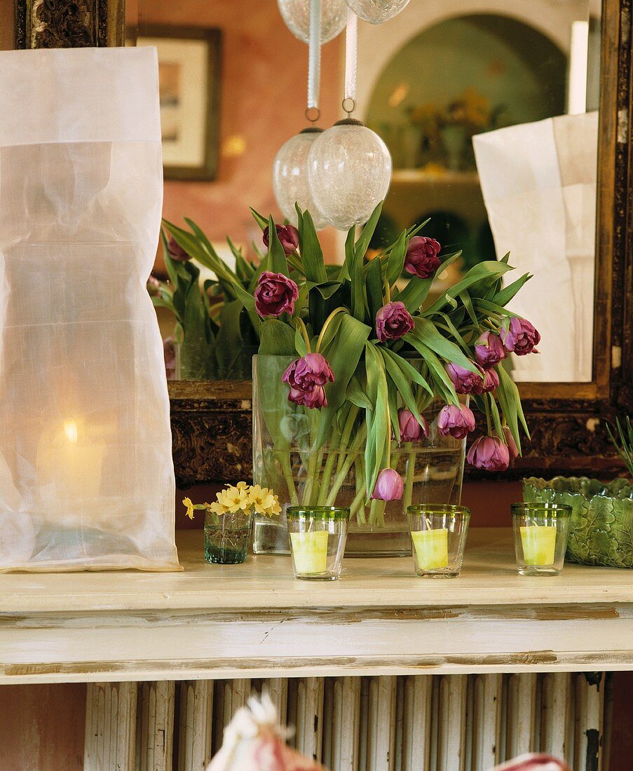 Violette Tulpen in Glasvase und Windlichter auf weisser Ablage