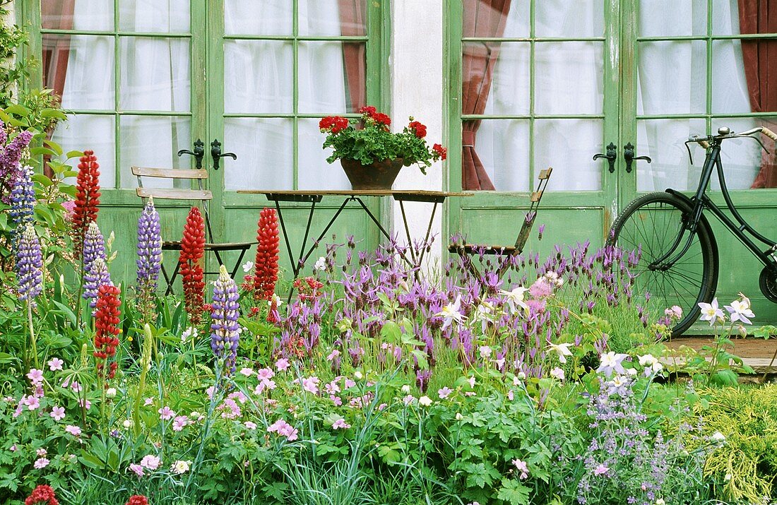 Blühender Garten mit Tisch und Stühlen vor Terrassentüren