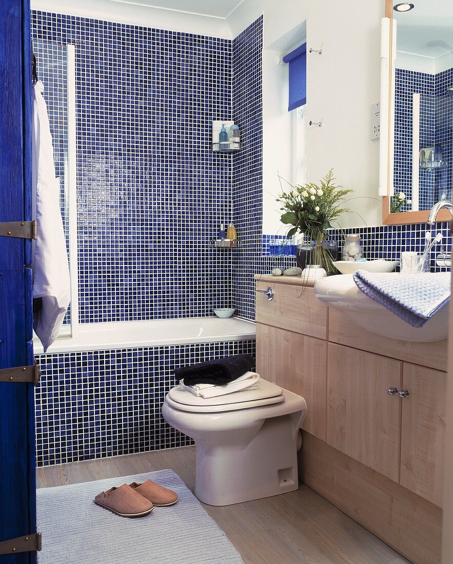 Badewanne vor Wand mit blauen Mosaikfliesen und Waschtisch aus Holz