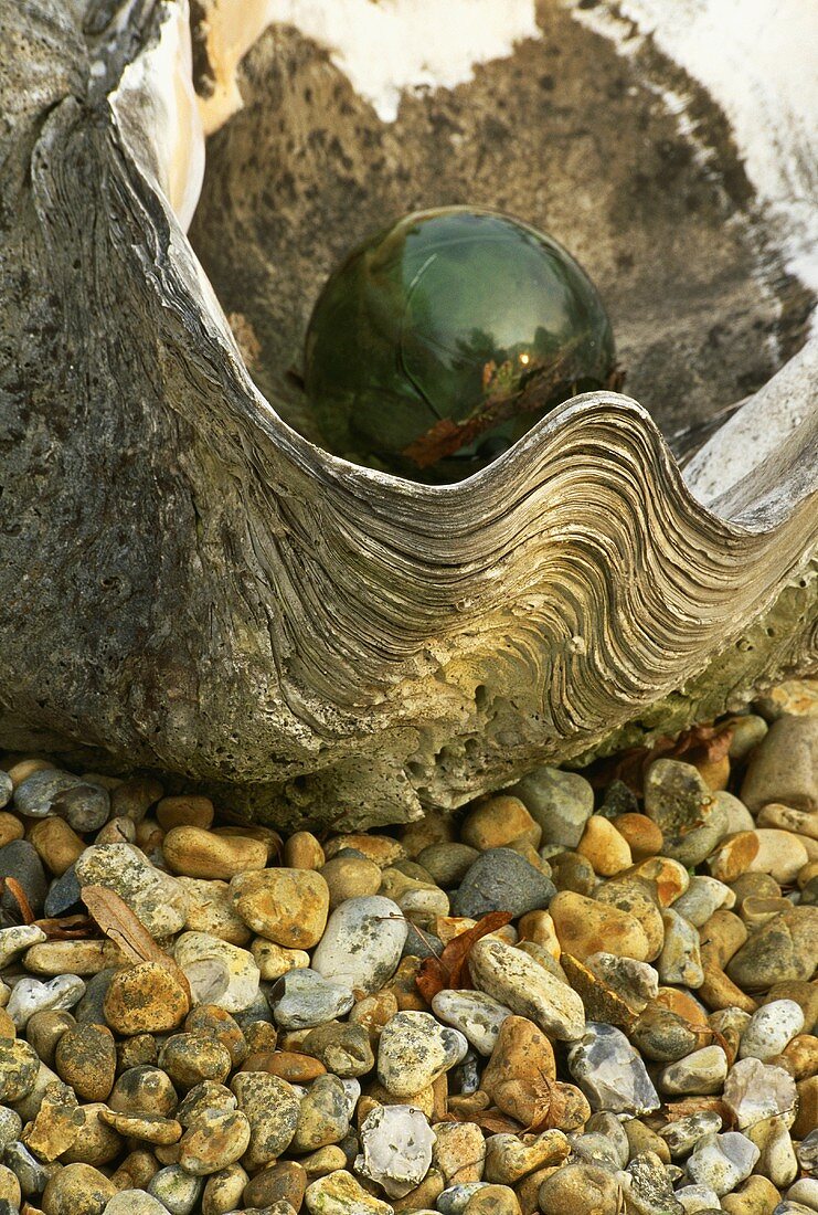 Grüne Glaskugel liegt in Muschel und auf Steinen