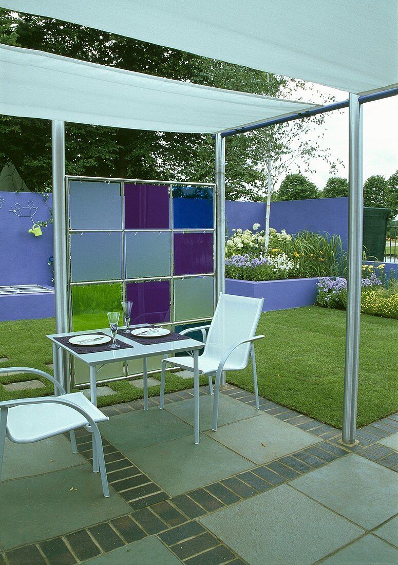 Terrassentisch und Stühle aus Metall unter moderner Pergola mit Gartenblick