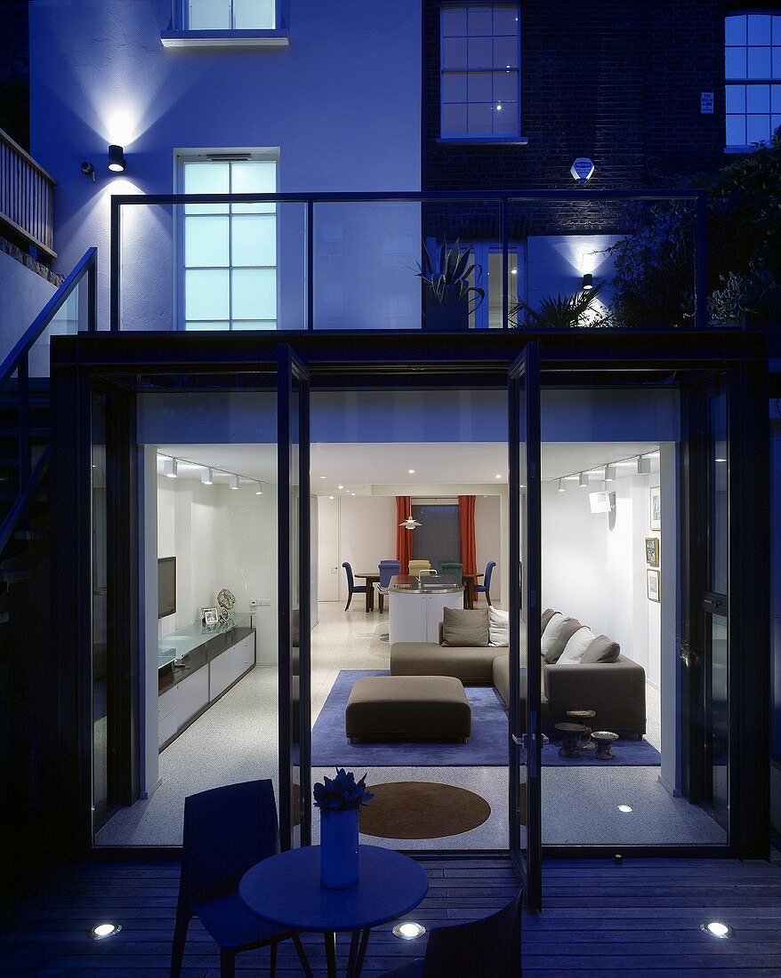 A terrace of a newly built house in the evening with an illuminated living room