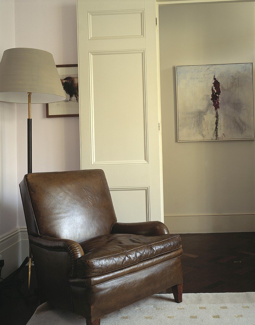 An old brown leather armchair in the corner of a living room next to an open door