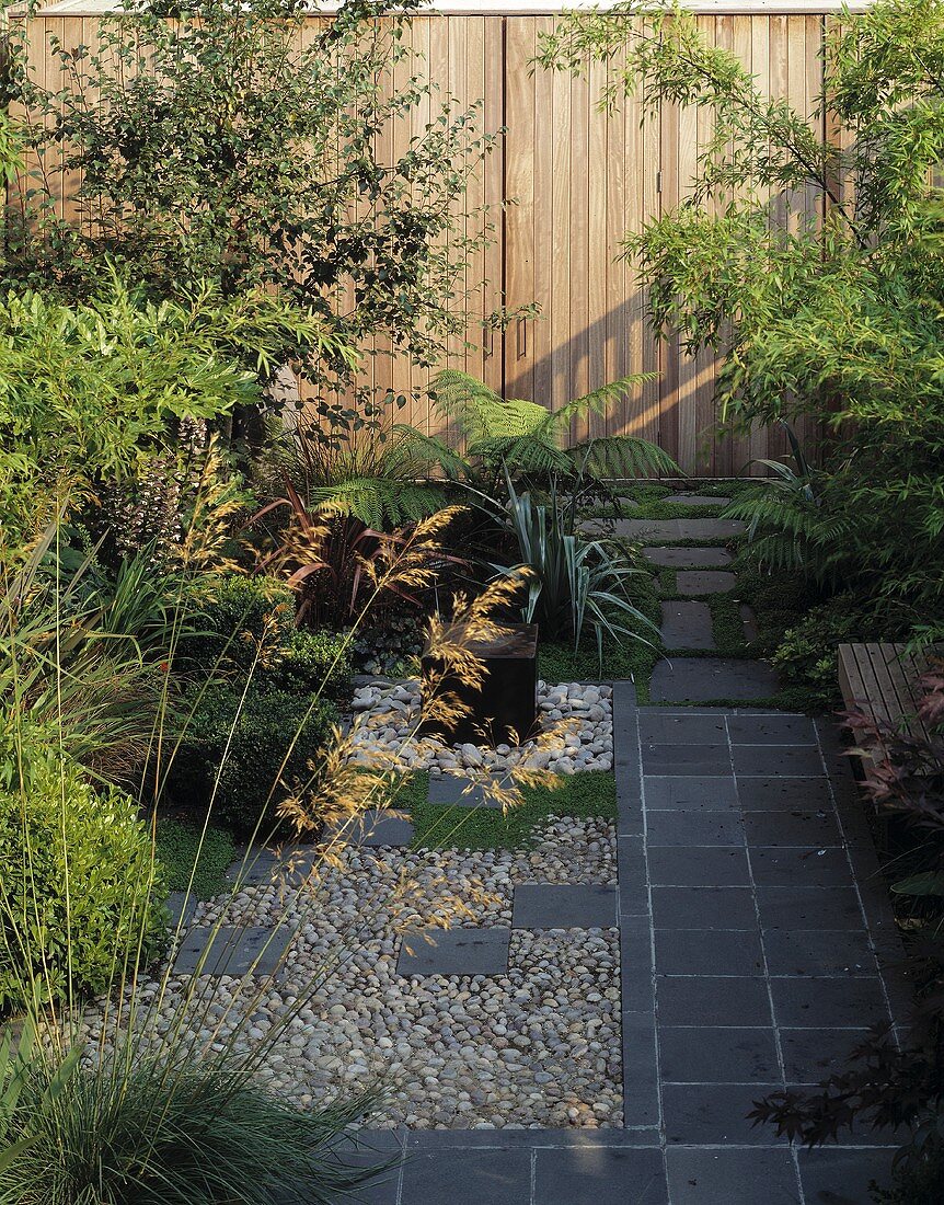 Sommerlicher Garten mit Weg aus grauen Steinplatten und Holzwand mit Tür