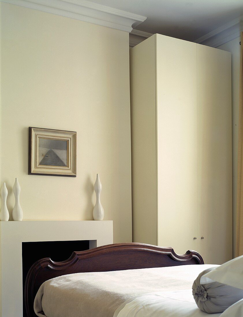 A simple bedroom with a modern wardrobe next to a fireplace and an antique bed