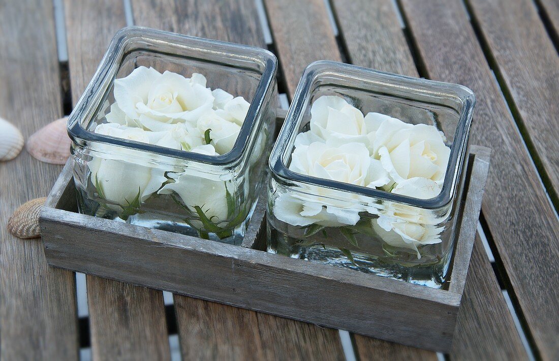 Rosenblüten in eckigen Glasbehältern auf Gartentisch