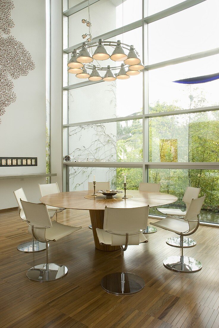 Designerlampe über Esstisch mit weissen Drehstühlen vor Glasfassade
