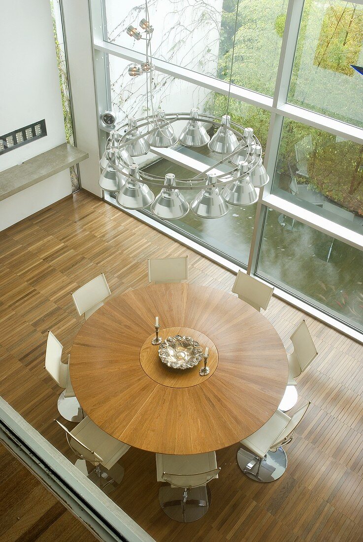 View of a round wooden table and white chairs in front a window bank in a modern living room
