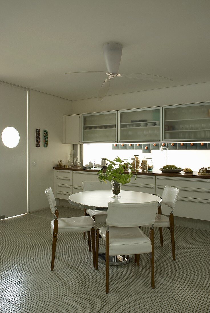 Esstisch mit gepolsterten Stühlen vor weisser Küchenzeile in moderner Küche