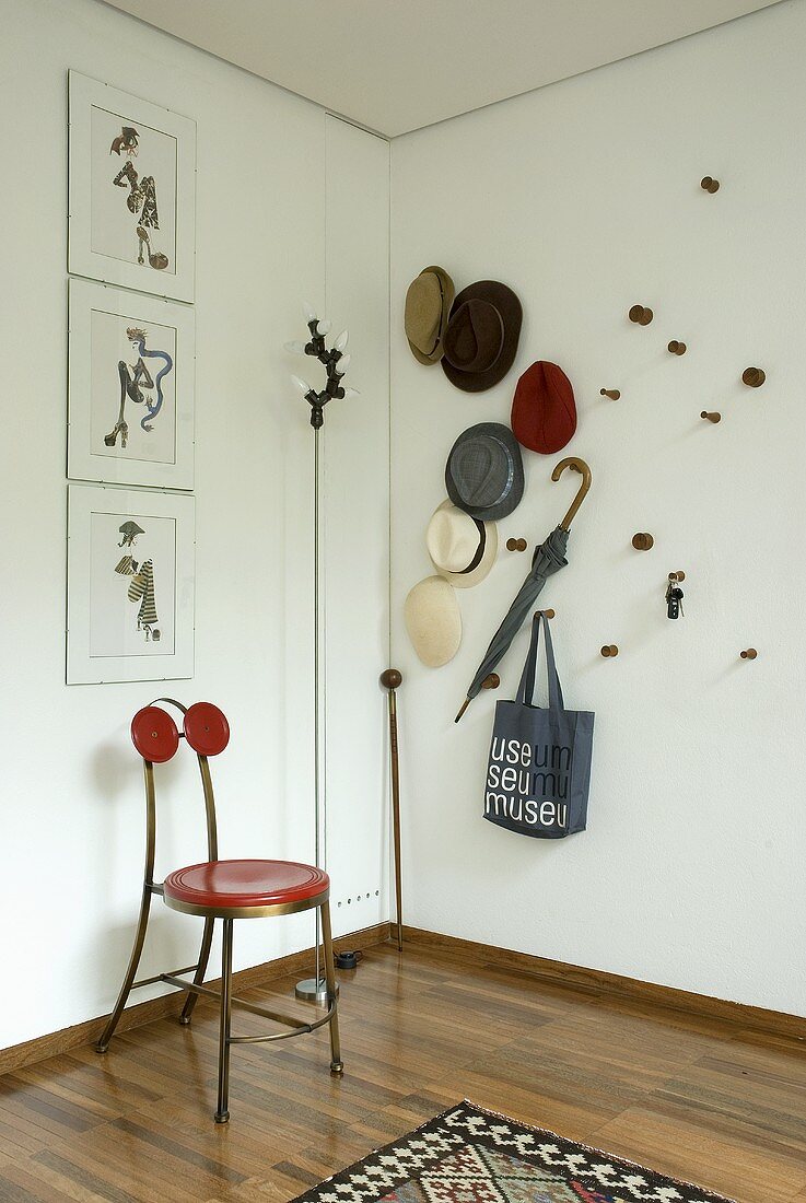 Zimmerecke mit Stuhl aus Metall und roter Sitzfläche neben Hutsammlung an Wand