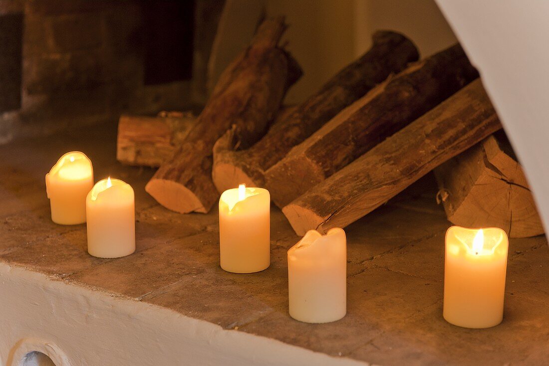 Brennende Kerzen und Holzscheite vor einem Kamin