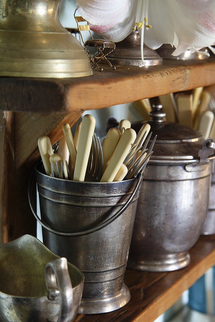 Knives and forks in a silver pot on a wooden shelf
