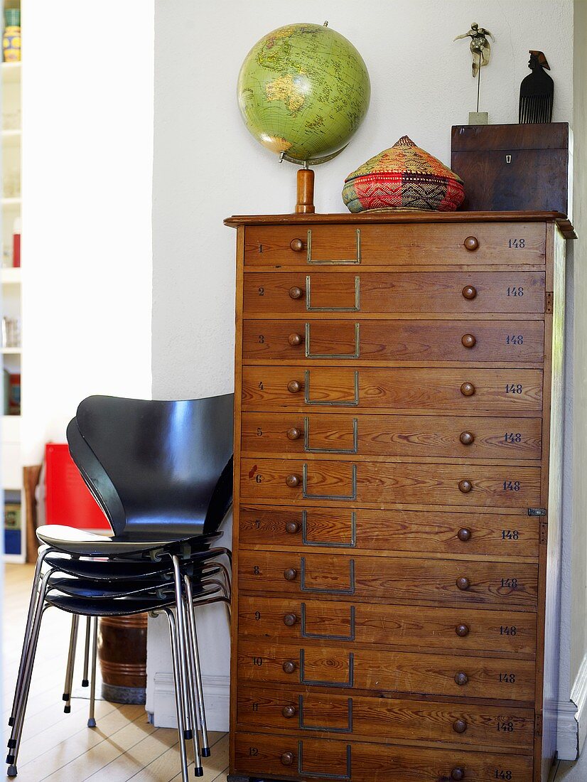 A globe on top of a chest of drawers with a stack of butterfly chairs beside it