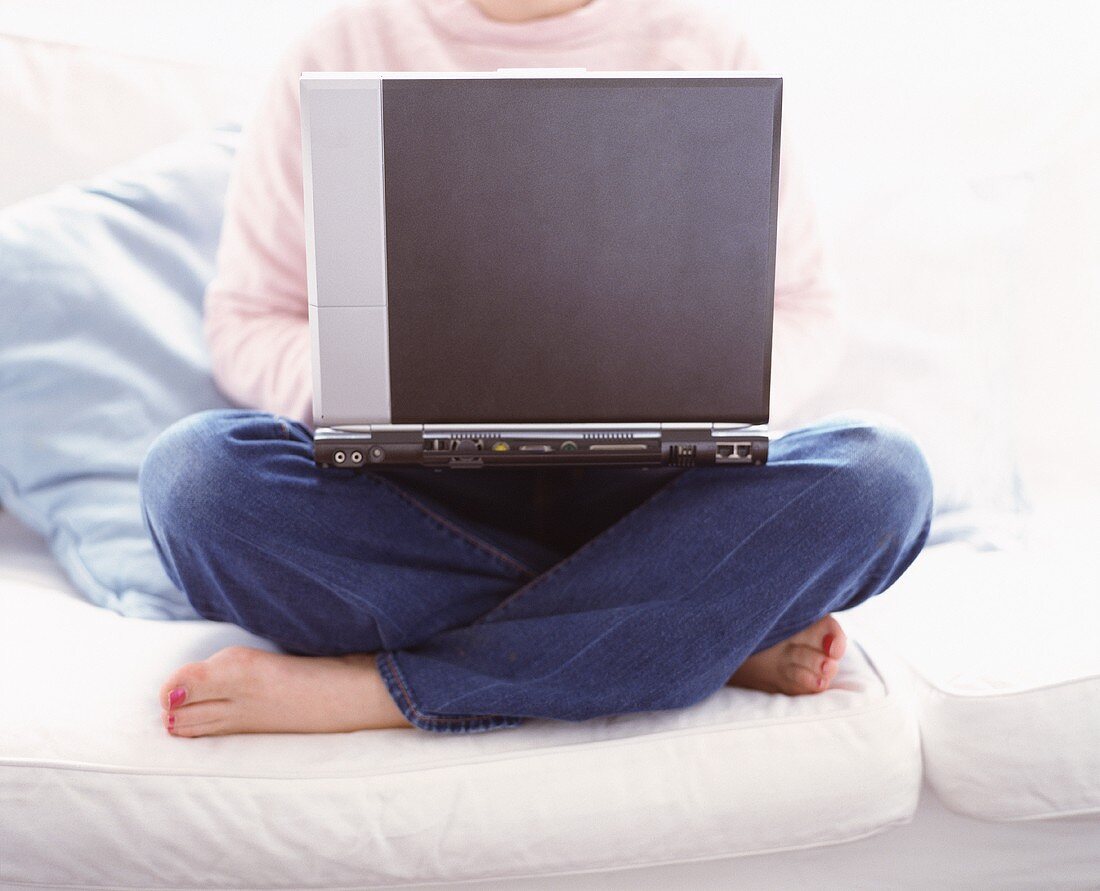 Frau mit Laptop auf den Knien am Sofa