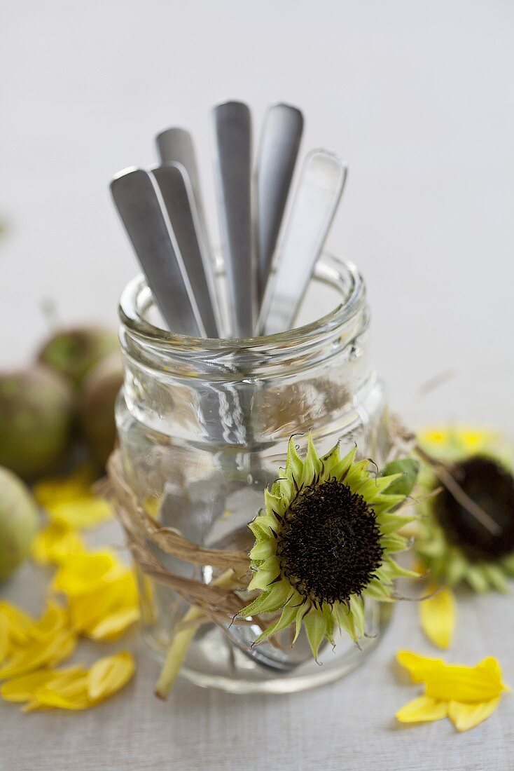 A glass of cutlery decorated with sunflower seed heads