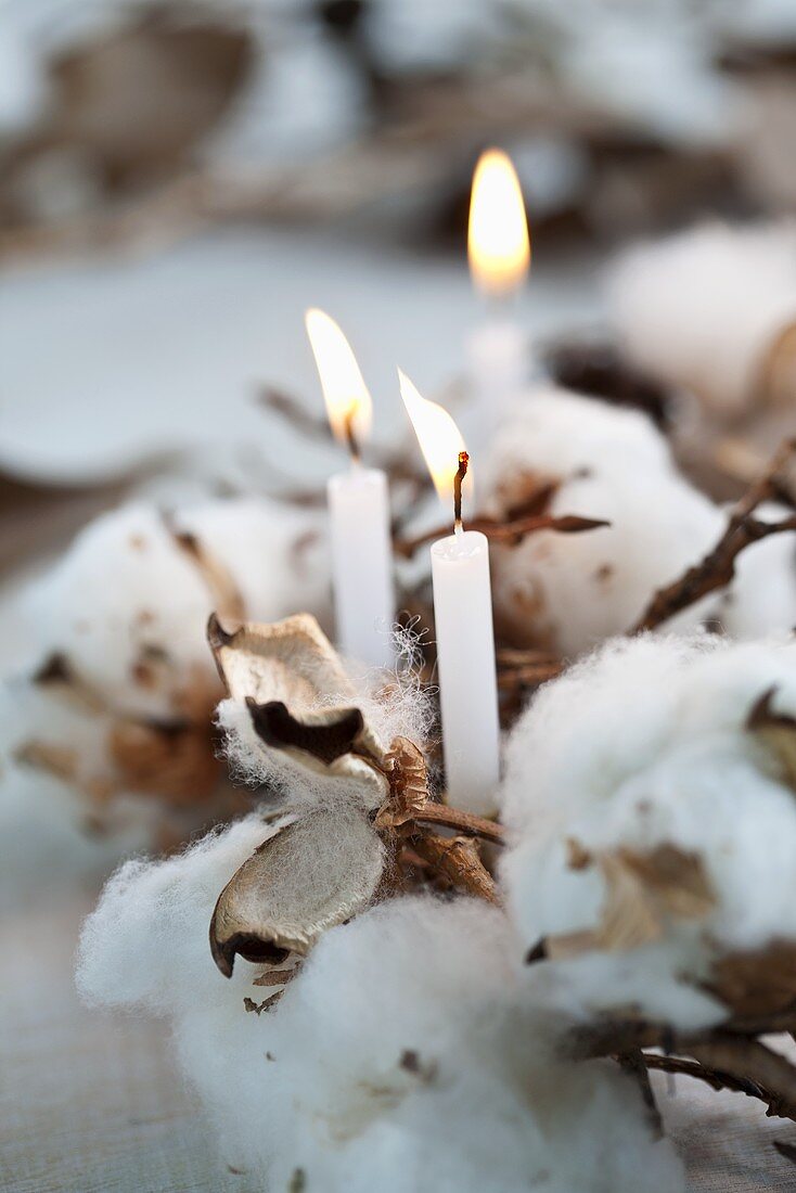 A wintry wreath made of cotton, cones and a candle (close-up)