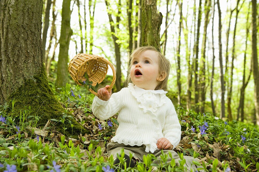 Kleines Kind mit Körbchen auf Waldboden sitzend