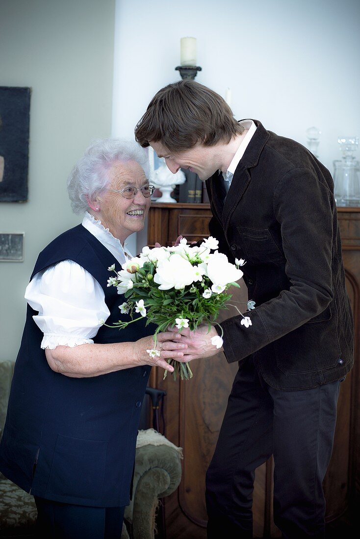 A grandson giving his grandmother a bunch of flowers for her birthday