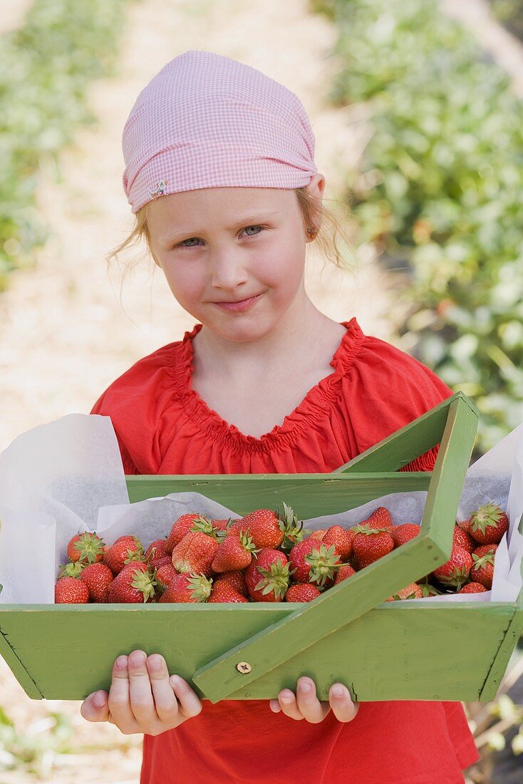 A girl holding a wooden basket of strawberries