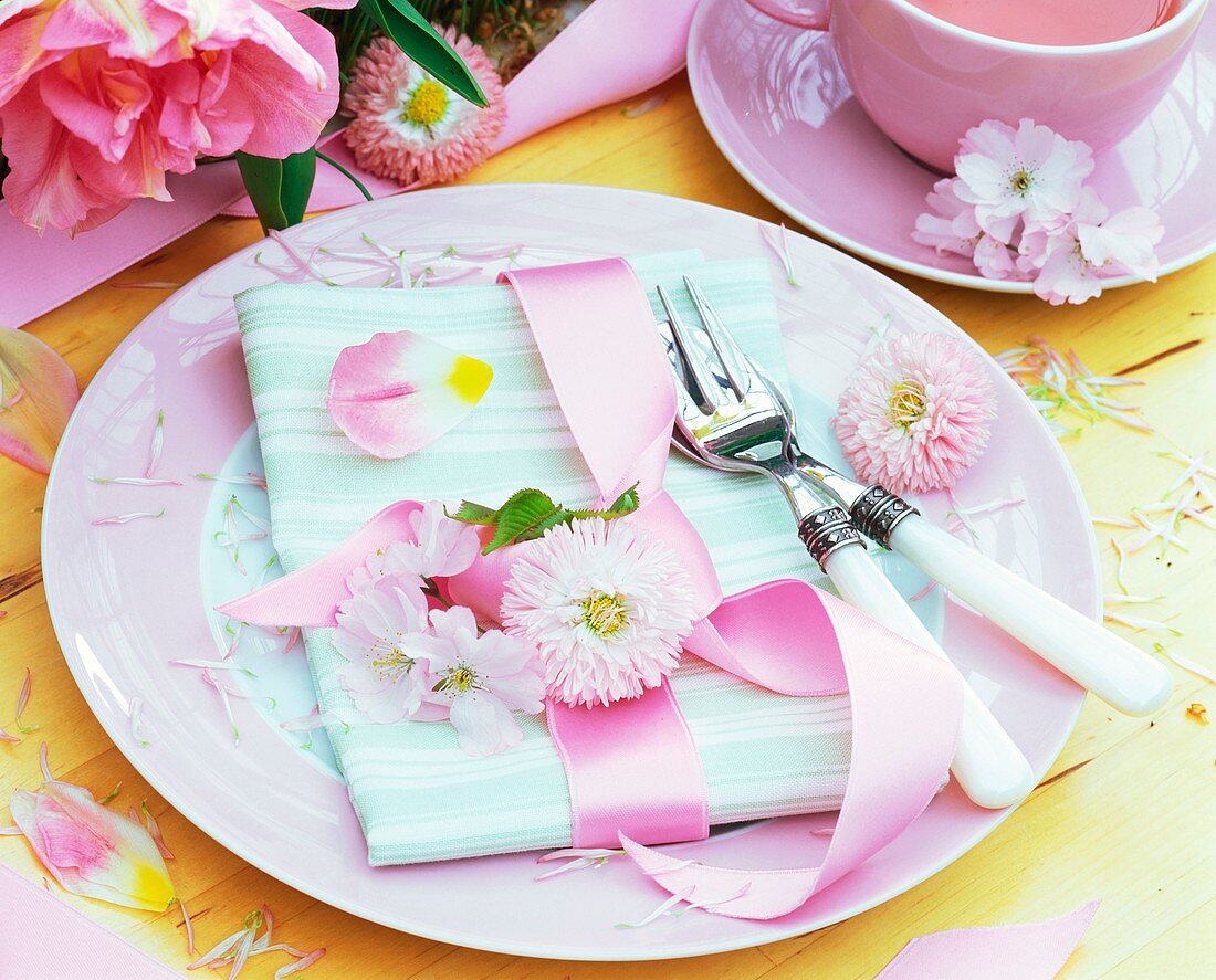 Place-setting with pink Bellis, fabric napkin and ribbon