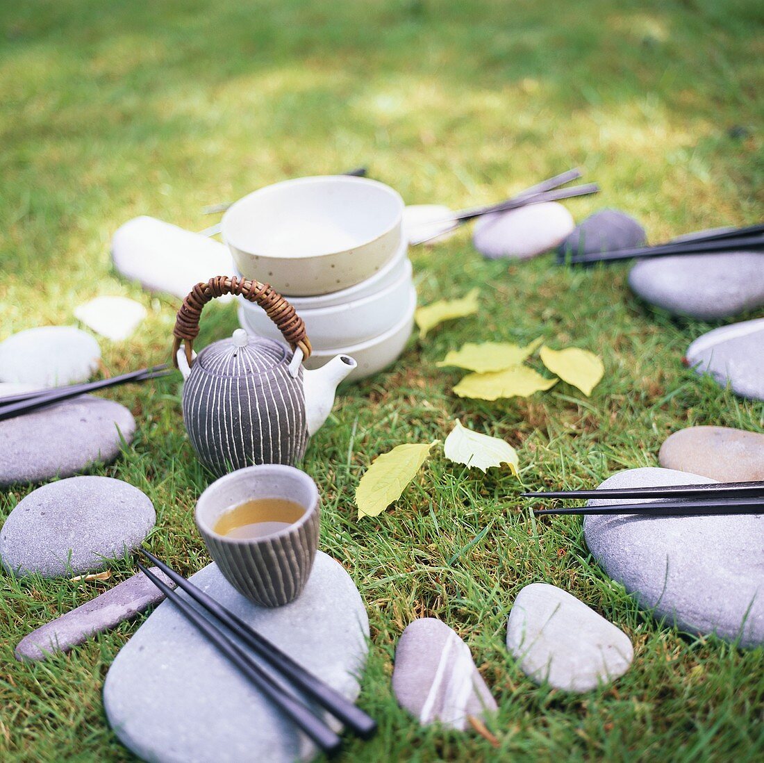 Stillleben mit Tee, Essstäbchen und Steinen im Freien