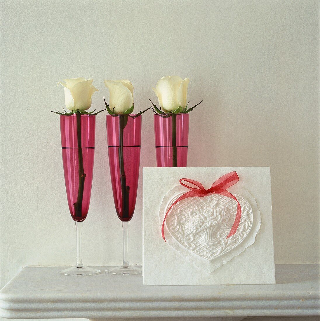 Three white roses in pink champagne glasses