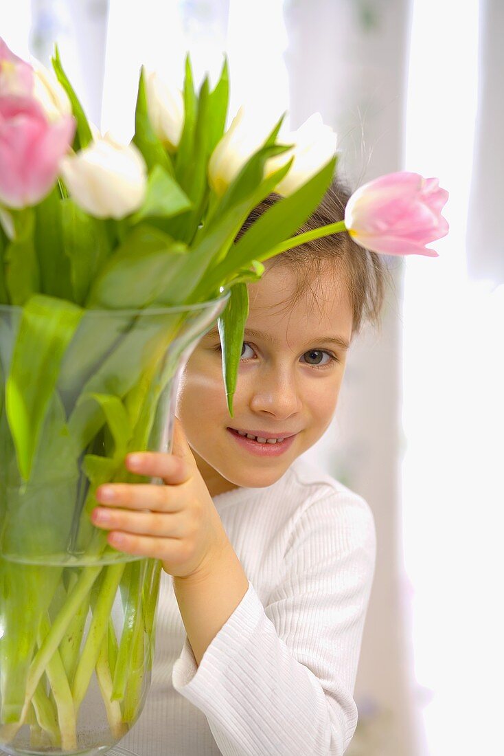 Mädchen versteckt sich hinter Vase mit Tulpenstrauss