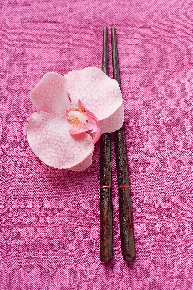 Essstäbchen und Orchidee auf pinkfarbenem Stoff