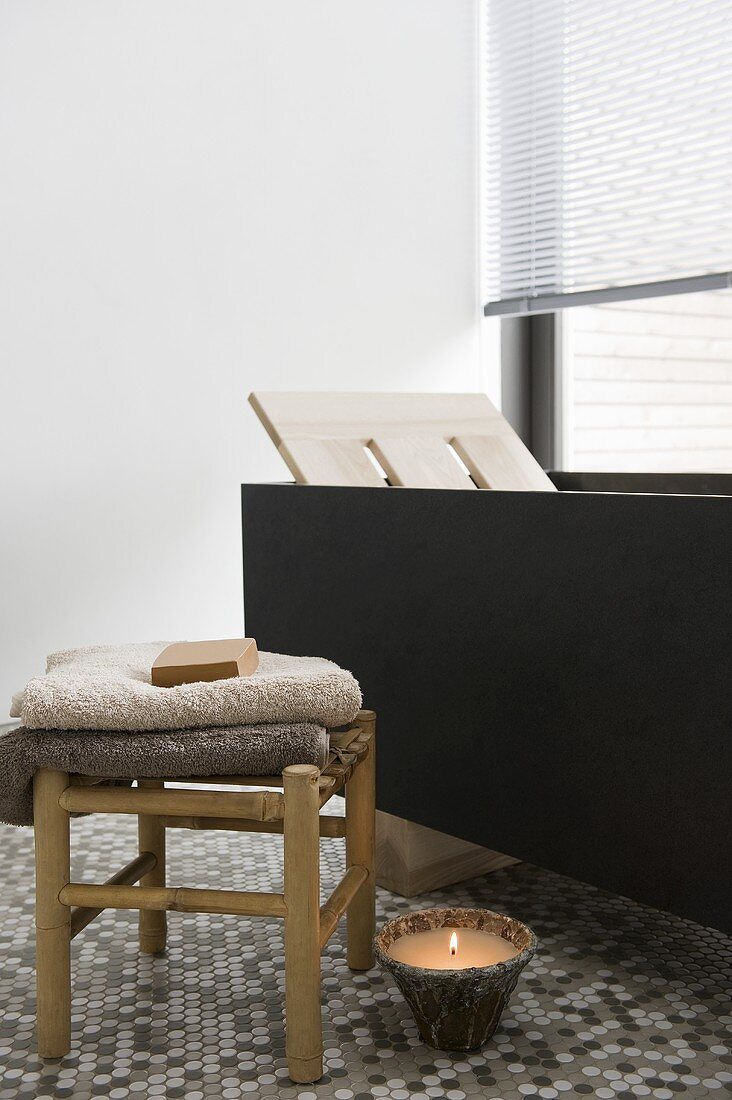 Badezimmer mit moderner freistehender Badewanne, Mosaikfliesenboden, Bodenkerze & Holzhocker mit Handtüchern