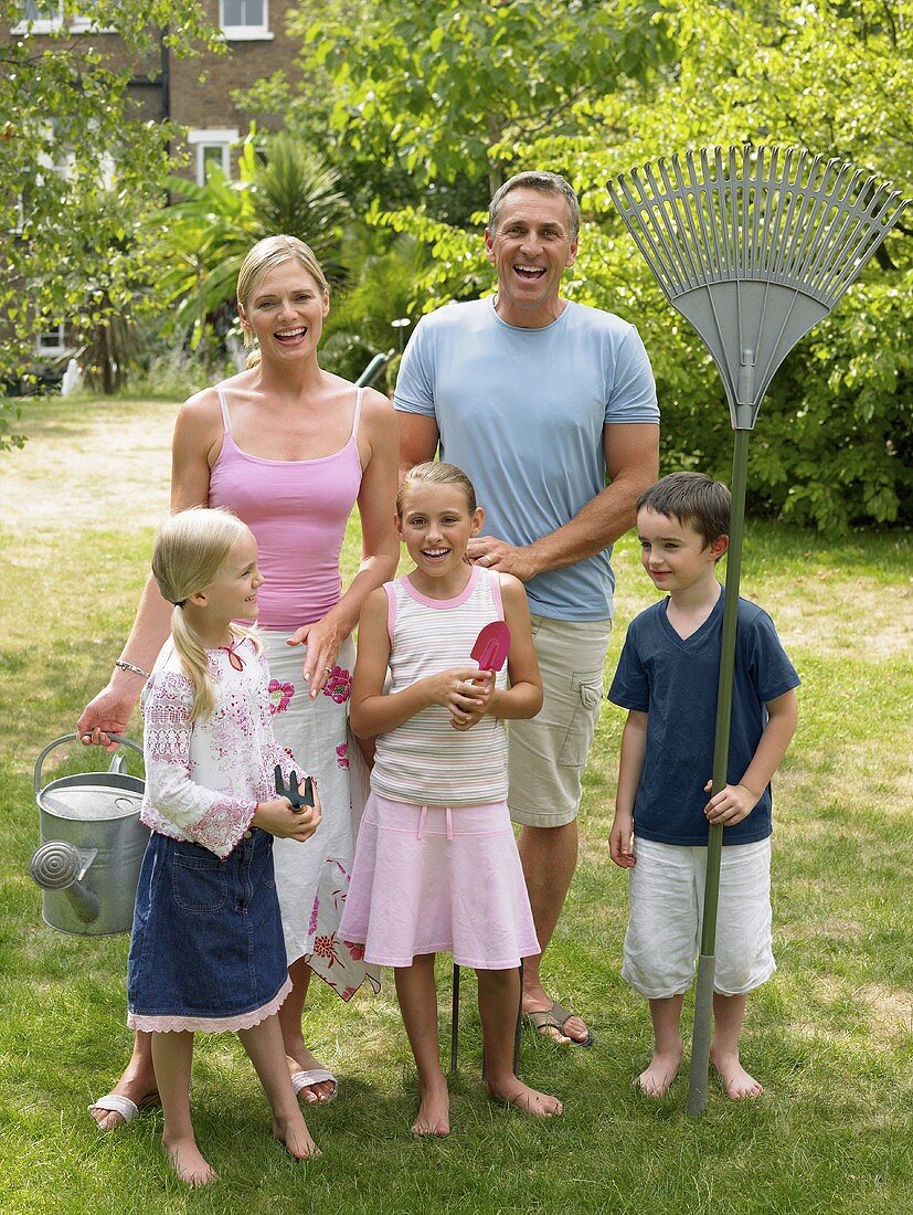 A family standing in garden holding gardening tools