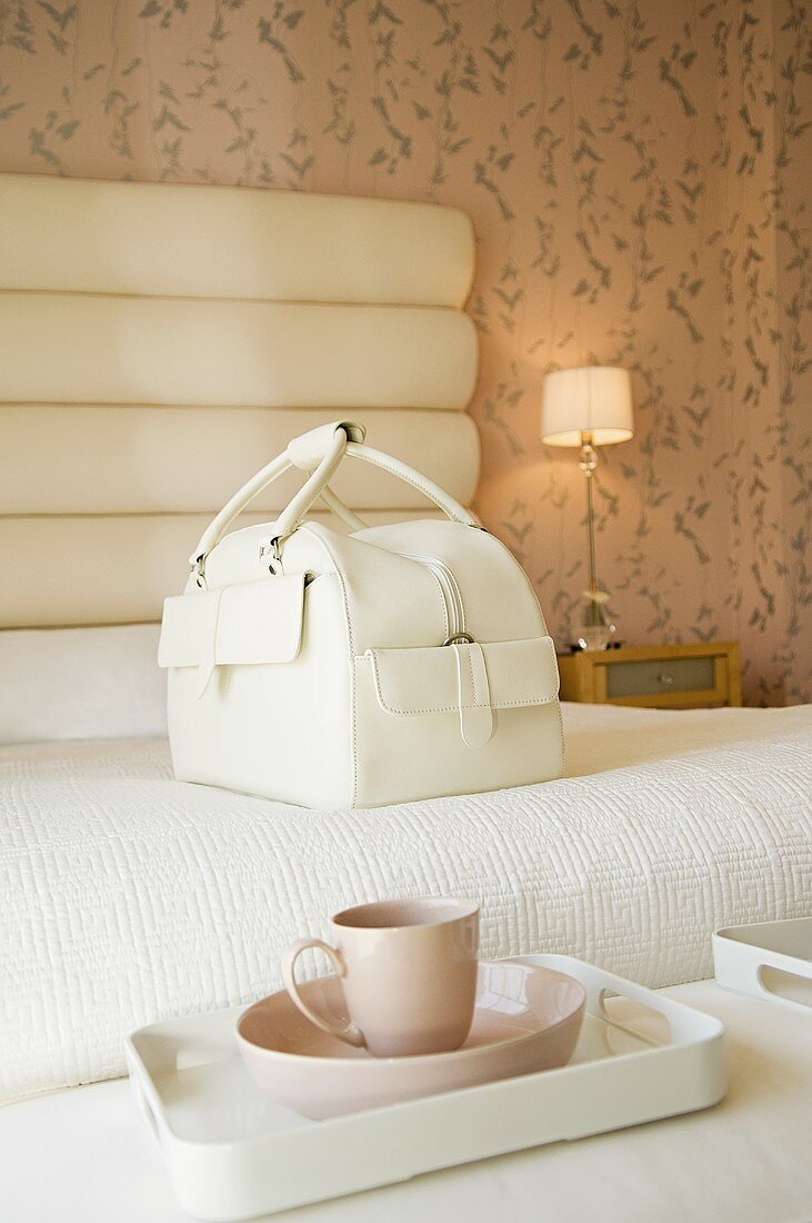 weiße Damentasche & Tablett mit Kaffeetasse auf einem Bett