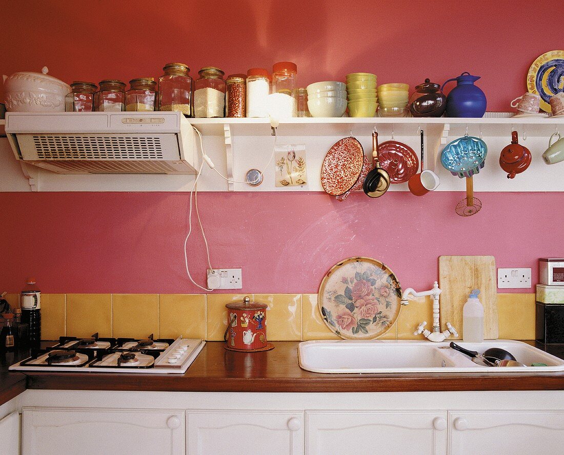Einfache Küche im Vintagelook mit Gasherd, weißem Spülbecken und Regal mit Geschirr und Lebensmitteln