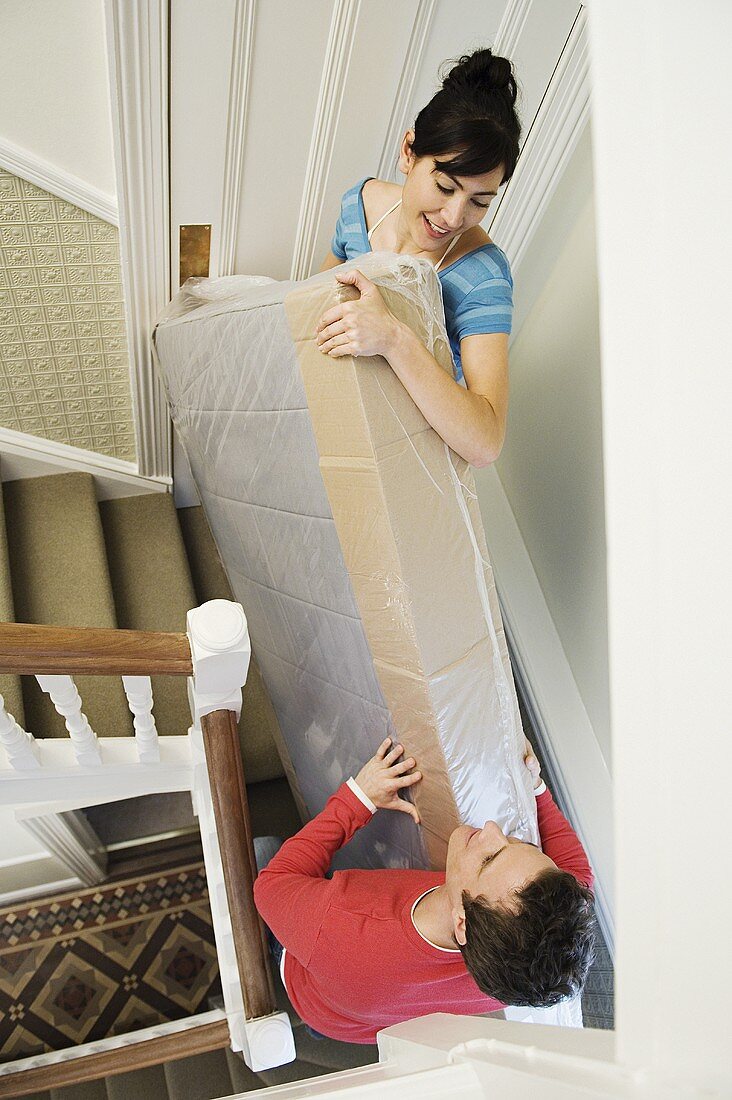 Pärchen trägt eine Matratze die Treppe hinauf