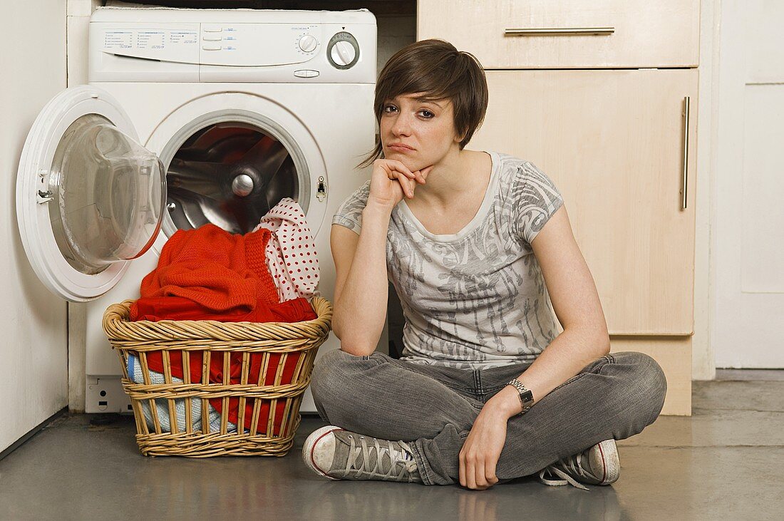 A young woman sitting in front of a washing machine
