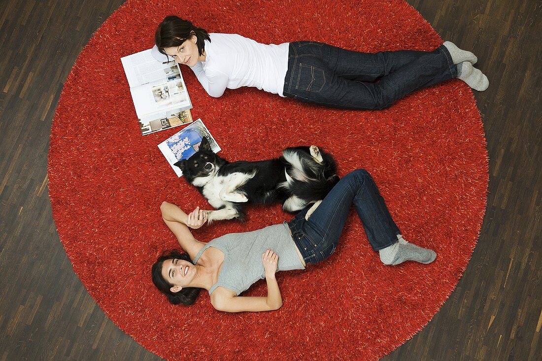 Frauen und Hund liegen auf Teppich
