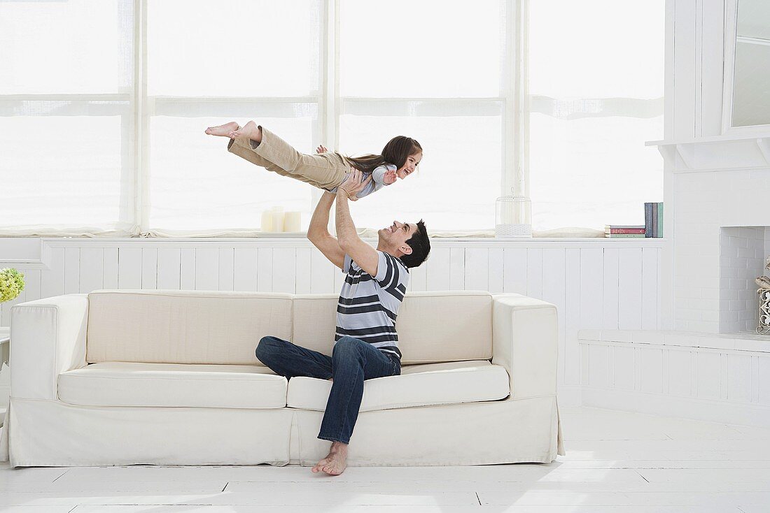 Vater spielt mit seiner kleinen Tochter in großem Raum mit Indurstriefenster
