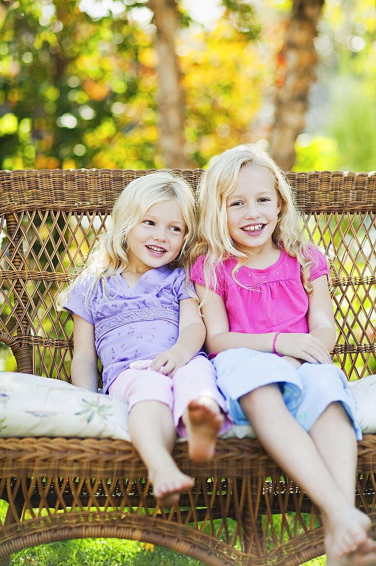 Schwestern sitzen auf Bank im Garten