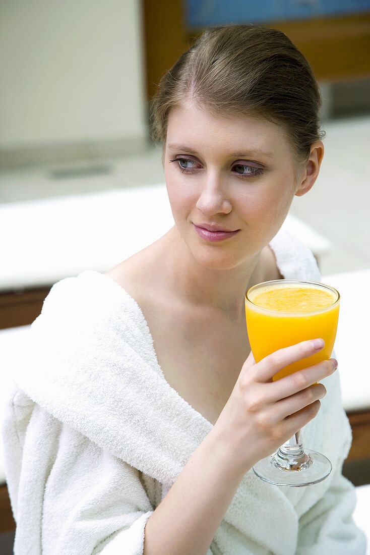 Junge Frau im Bademantel trinkt Orangensaft