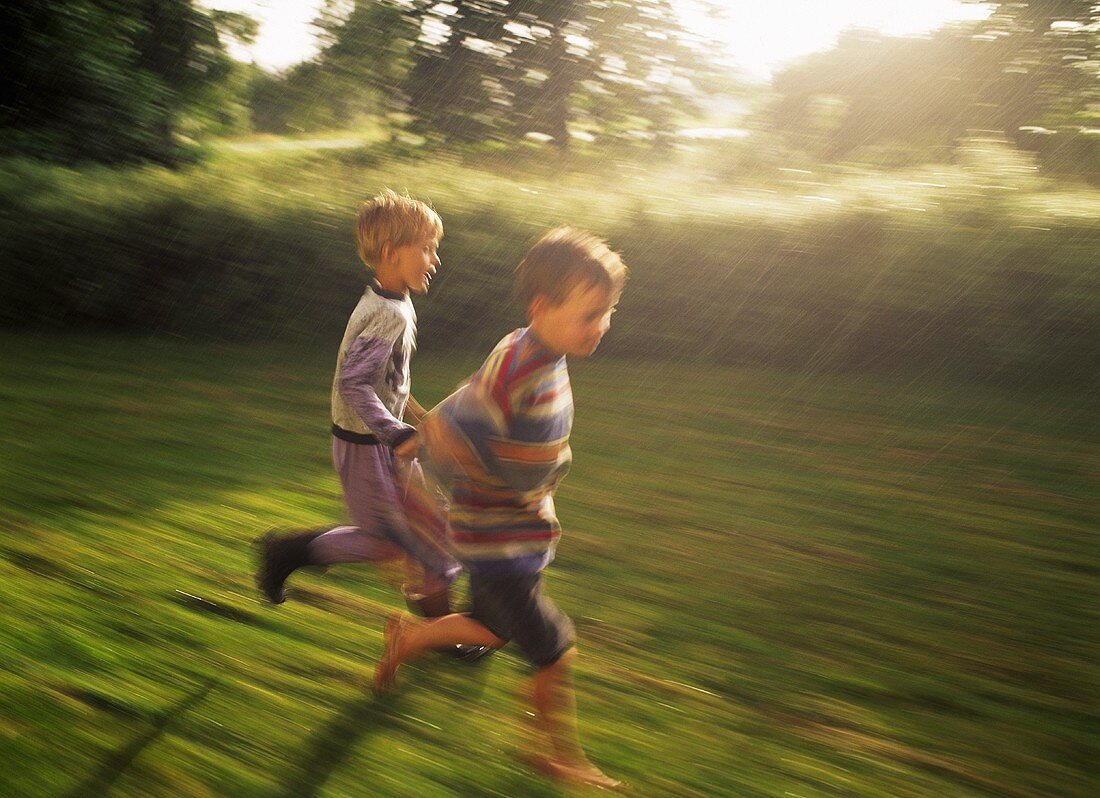Zwei kleine Jungen laufen im Regen auf der Wiese
