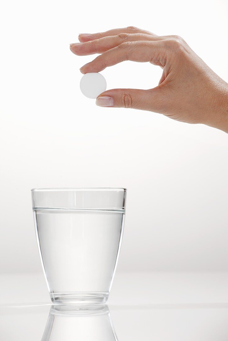 A hand holding an effervescent tablet over a glass