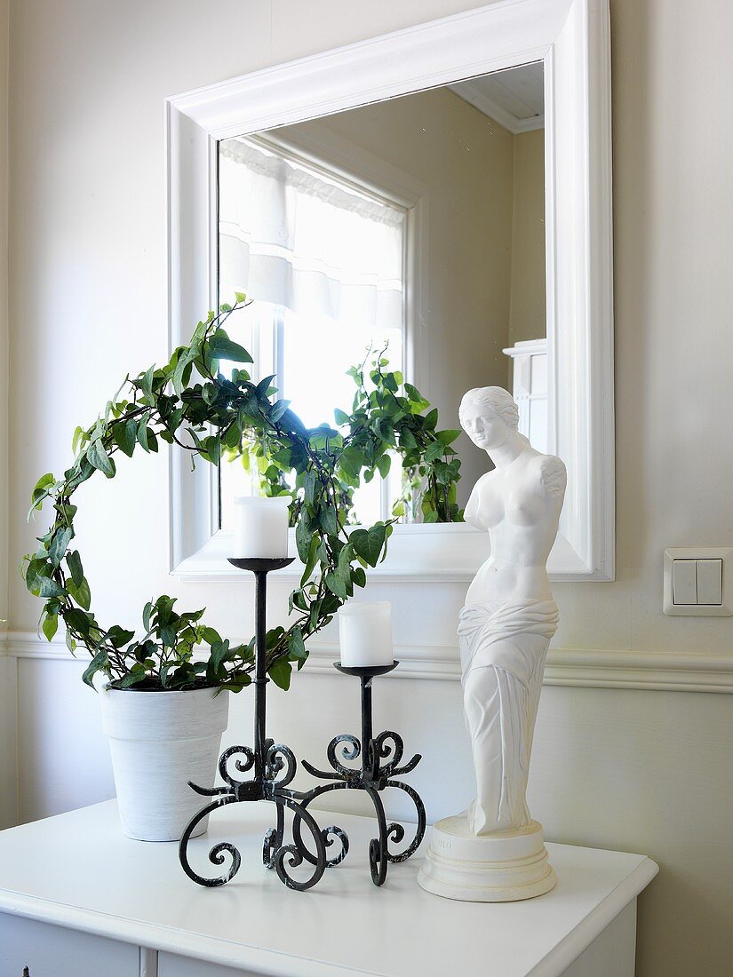 Venus-Statue, Kerzenhalter und Pflanzendekoration auf weißem Garderobentisch vor Spiegel