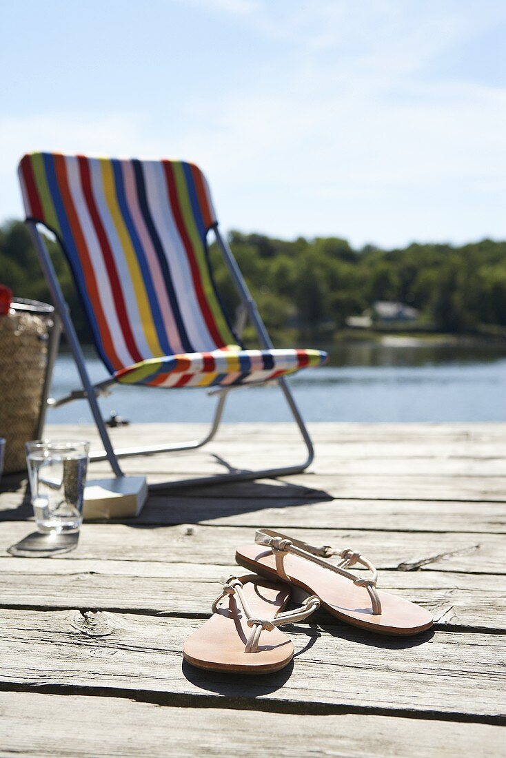 Sonnenstuhl und Flip Flops auf Holzsteg am See