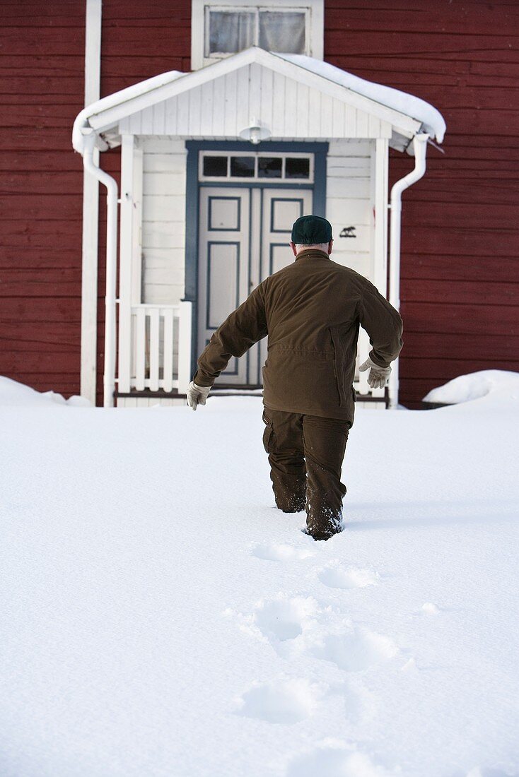 Mann läuft durch tiefen Schnee zum Haus