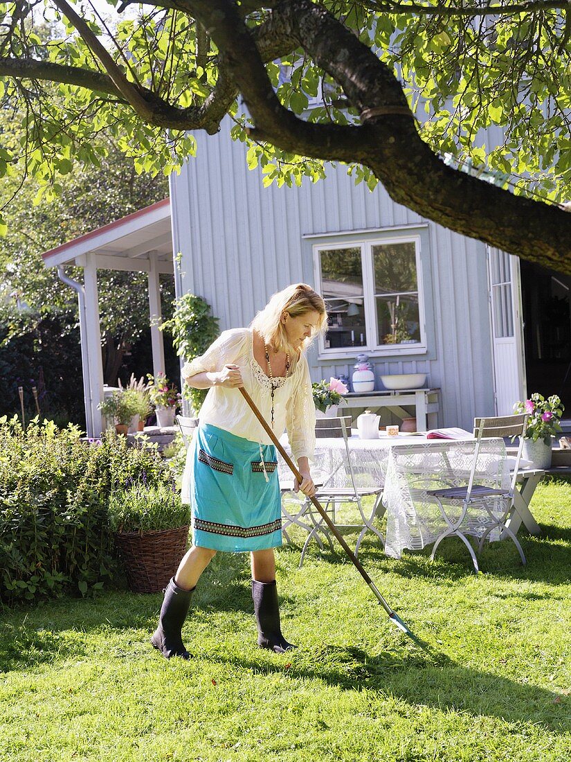 Woman raking up grass clippings in garden