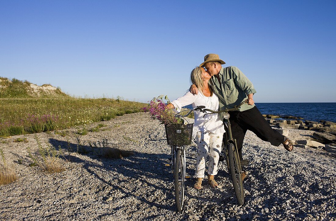 Älteres Pärchen mit Fahrrädern küssen sich am Strand