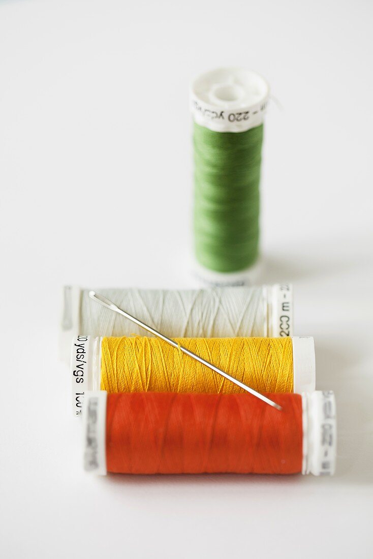 Four different spools of thread and a sewing needle